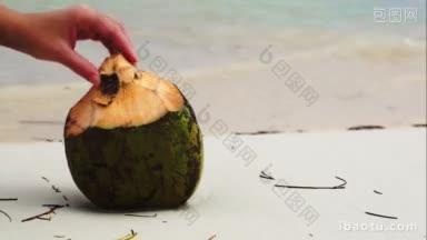 特写镜头的女手把一根吸管放在椰子躺在海滩<strong>水</strong>冲洗它